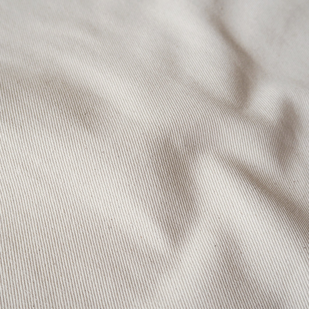A close-up of a light beige fabric with a fine twill texture and soft shadows in the folds.