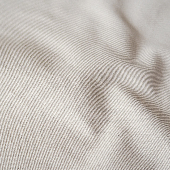 A close-up of a light beige fabric with a fine twill texture and soft shadows in the folds.