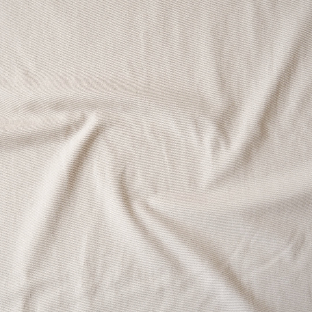 A close-up of draped off-white fabric with soft folds and a slightly textured surface.