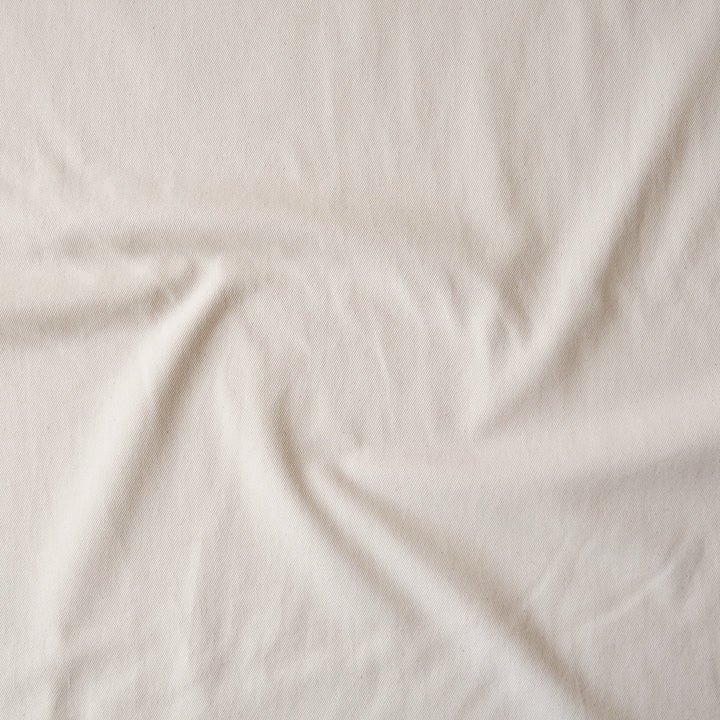 A close-up of draped off-white fabric with soft folds and a slightly textured surface.