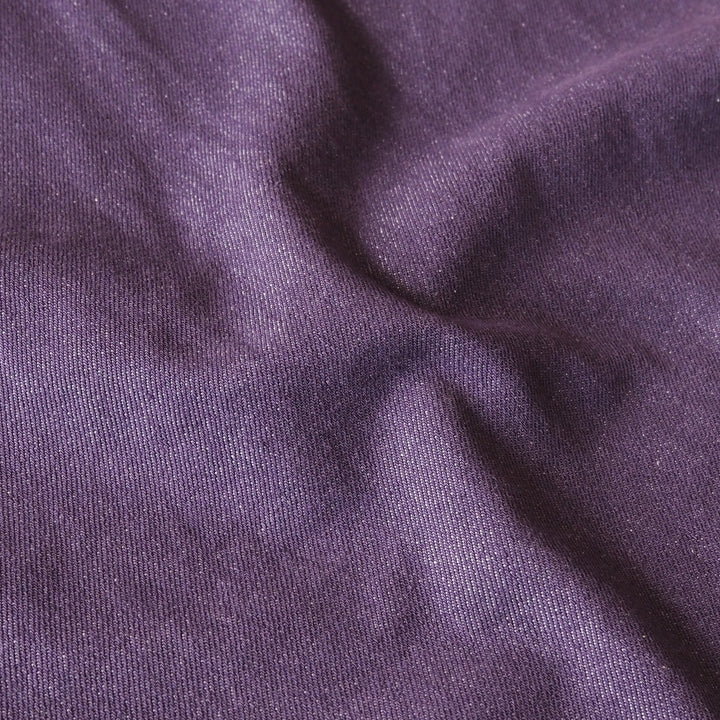 A close-up of draped purple denim fabric with a fine twill texture and soft folds.