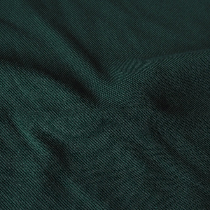 A close-up of dark teal-green ribbed fabric texture with soft folds and shadows.