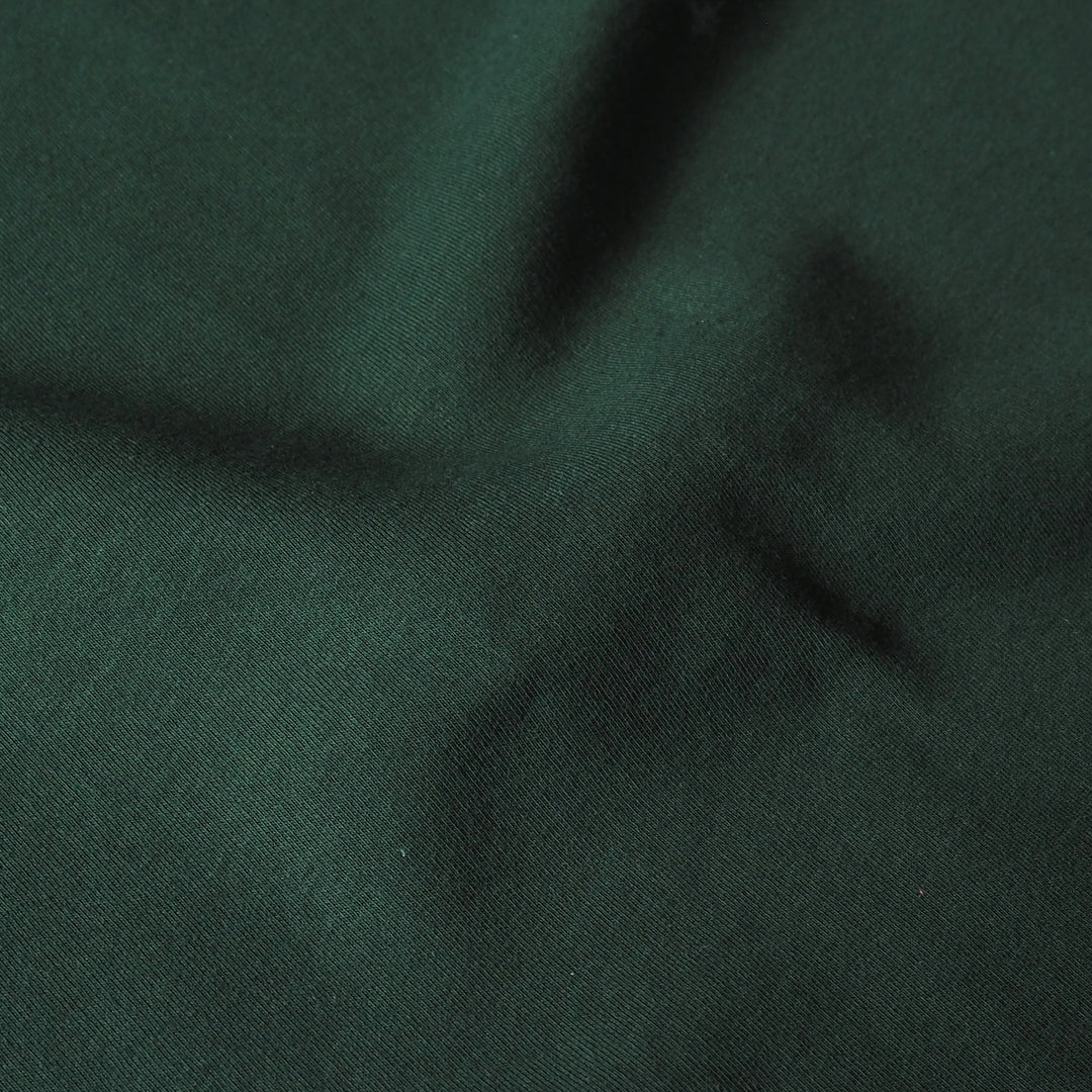 A close-up of dark forest green textured fabric with soft folds and shadows.
