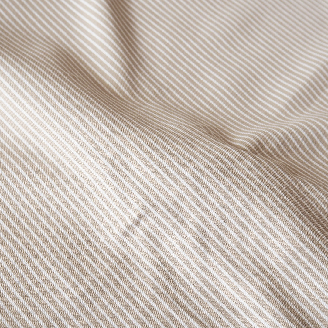 A close-up of draped fabric with a fine diagonal stripe pattern in warm beige and off-white.