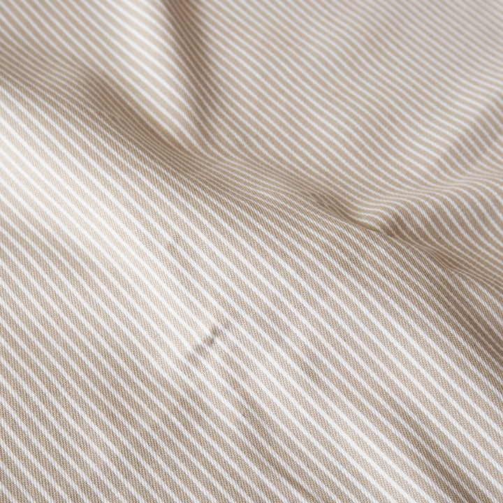 A close-up of draped fabric with a fine diagonal stripe pattern in warm beige and off-white.