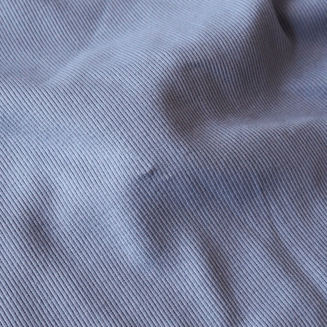 A close-up of a light blue-gray ribbed fabric with a fine vertical stripe texture and soft folds.
