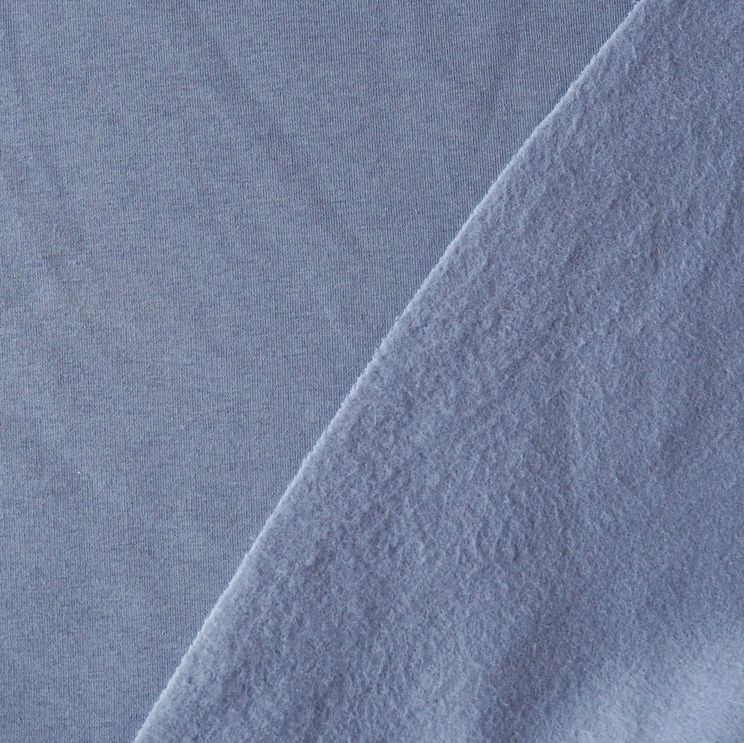 A close-up of light periwinkle blue fabric with a diagonal fold showing the soft texture.