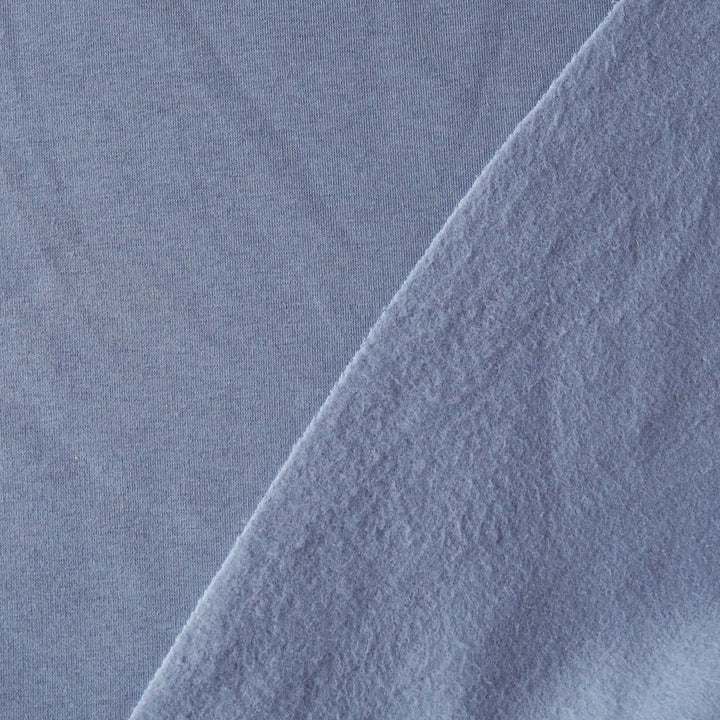 A close-up of light periwinkle blue fabric with a diagonal fold showing the soft texture.