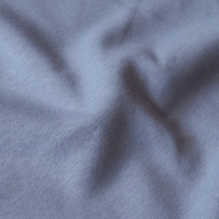 A close-up of draped slate blue fabric with a fine twill texture and soft folds.