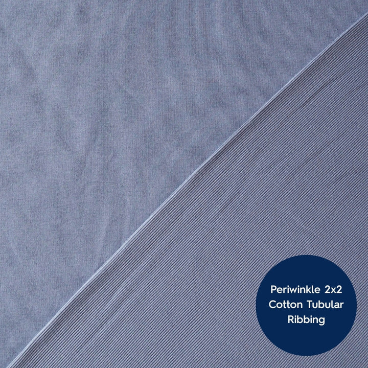 A close-up of periwinkle blue cotton tubular ribbed fabric, showing a diagonal fold line and a dark blue circular label with the text 'Periwinkle 2x2 Cotton Tubular Ribbing'.