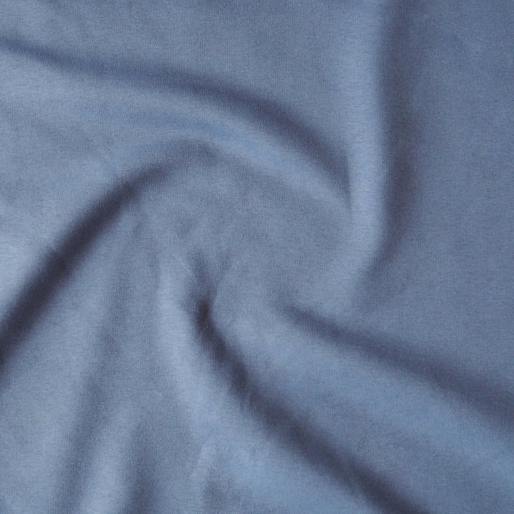 A close-up of draped dusty blue fabric with soft folds and a matte texture.