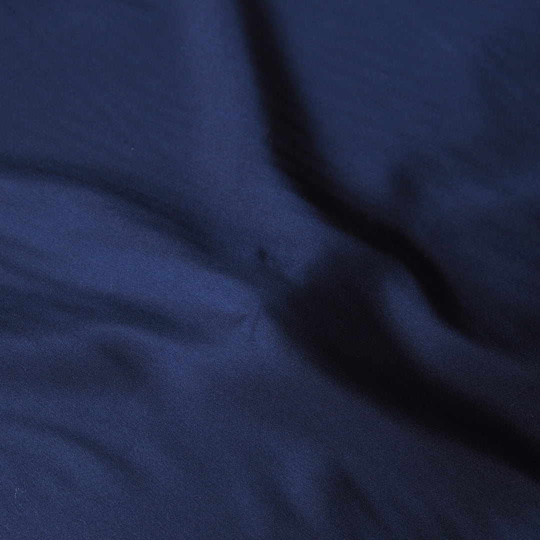 A close-up of dark navy blue fabric with soft folds and a subtle sheen.