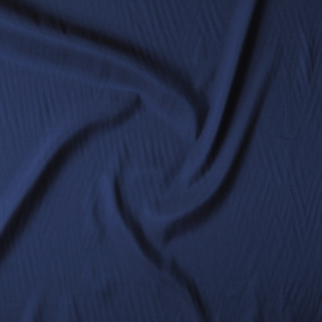 A close-up of dark blue textured fabric arranged in soft folds.