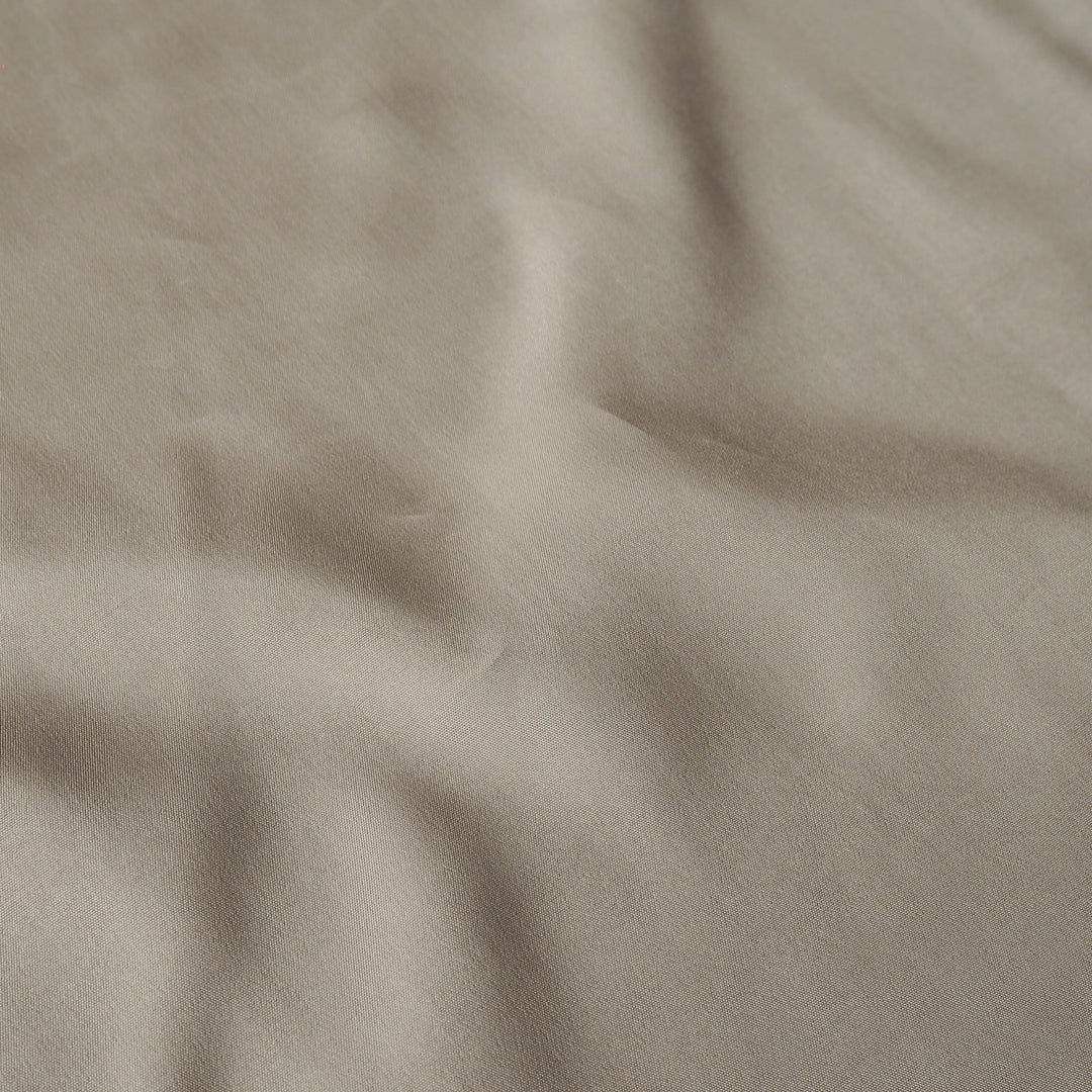 A close-up of draped fabric in a warm taupe-beige color, showing soft folds and texture.