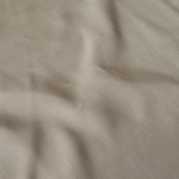 A close-up of draped fabric in a warm taupe-beige color, showing soft folds and texture.
