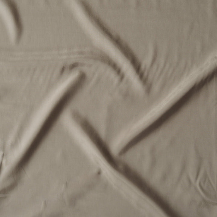 A close-up of a light taupe or beige textured material with a subtle woven or embossed pattern and soft shadows.