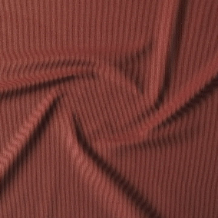 A close-up of draped ribbed fabric in a muted brick red or terracotta color, filling the entire frame.