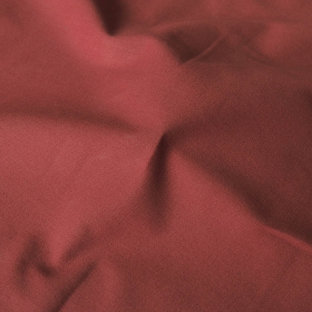 A close-up of draped dusty rose red fabric with soft folds and a fine woven texture.