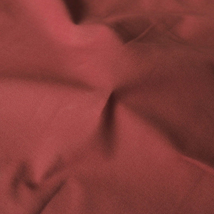 A close-up of draped dusty rose red fabric with soft folds and a fine woven texture.