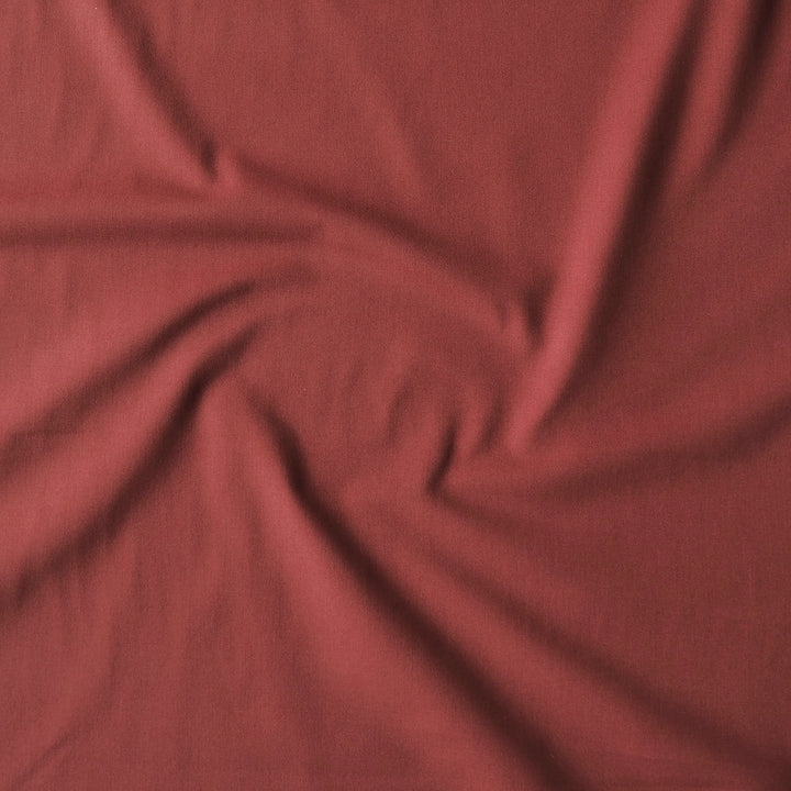 A close-up of draped dusty rose red fabric with soft swirls and folds showing its texture and color.