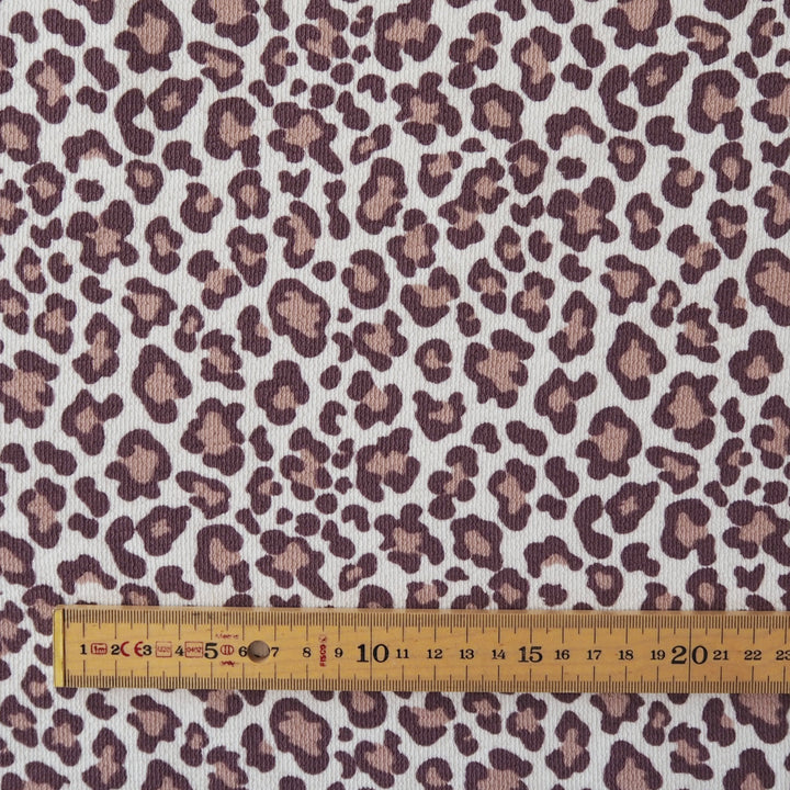 Leopard print fabric with brown and beige spots on a white background, shown with a wooden ruler at the bottom for scale.