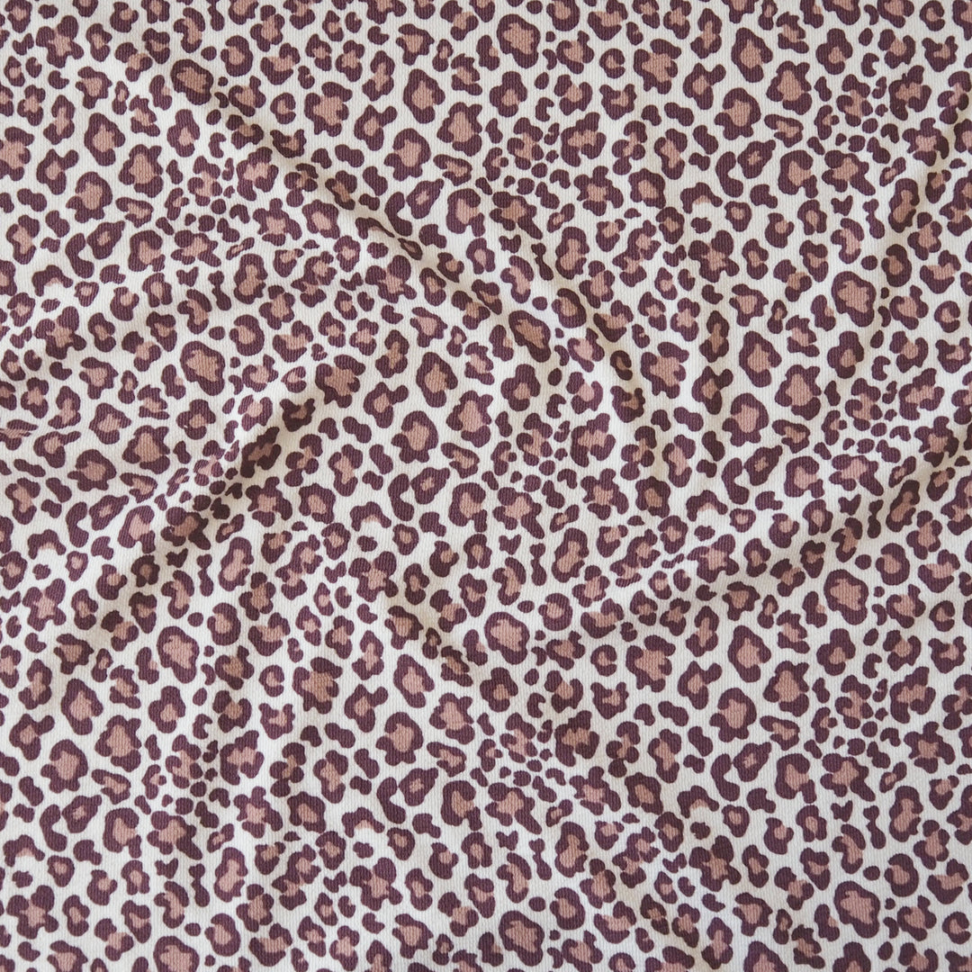 A close-up of leopard print fabric with a dusty rose and brown spot pattern on a white background.