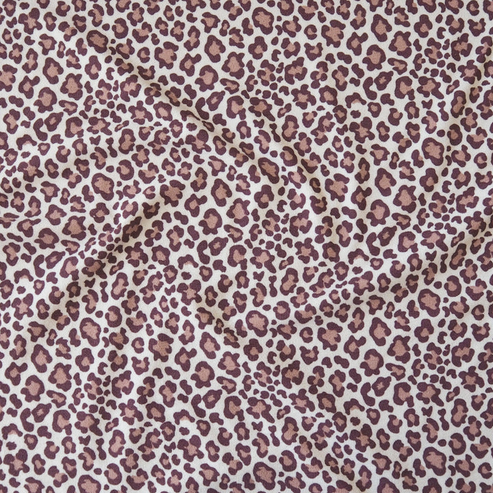 A close-up of leopard print fabric with a dusty rose and brown spot pattern on a white background.