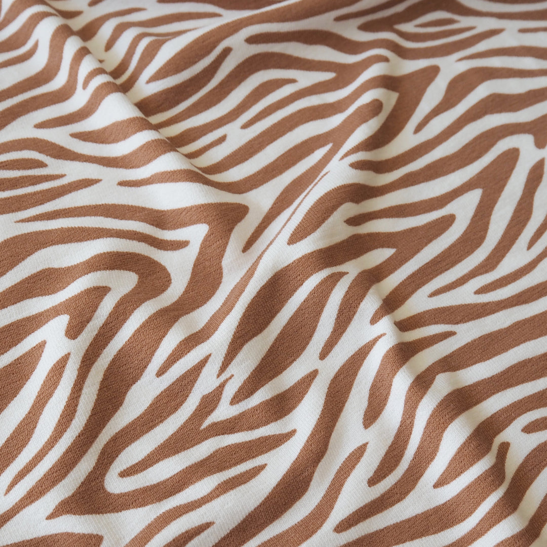 A close-up of draped fabric with a zebra-like abstract stripe pattern in warm brown on an off-white background.