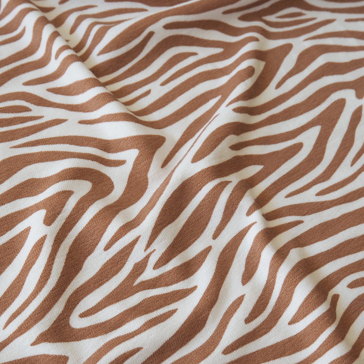 A close-up of draped fabric with a zebra-like abstract stripe pattern in warm brown on an off-white background.