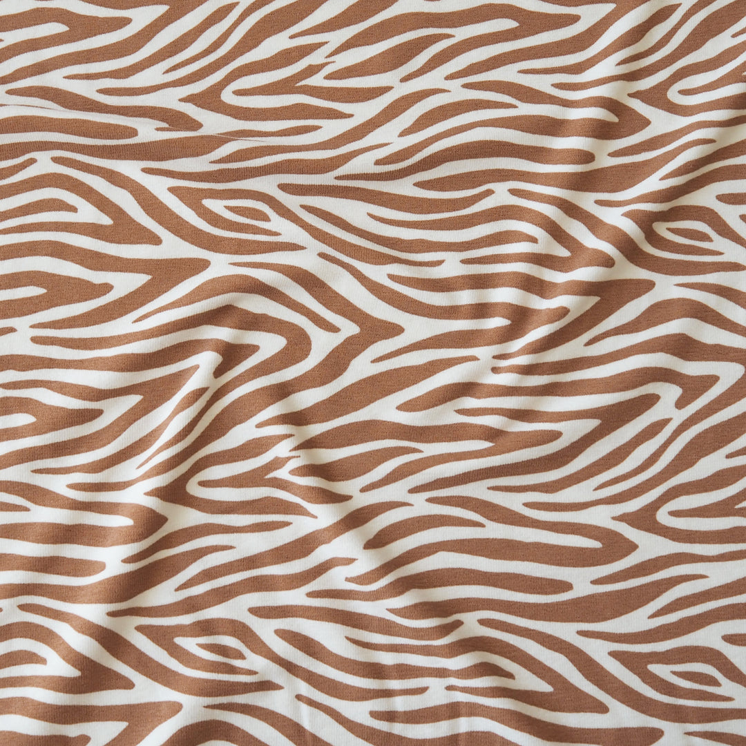 A close-up of a zebra-stripe patterned fabric with wavy brown lines on an off-white background, showing soft folds and texture.