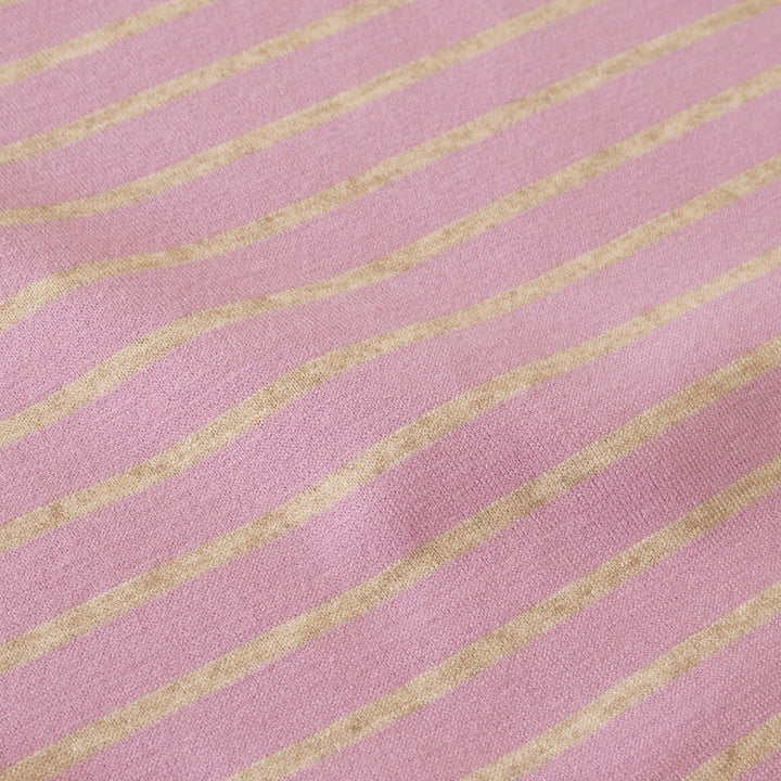 A close-up of pink fabric with repeating diagonal wavy stripes in a warm tan or beige tone.