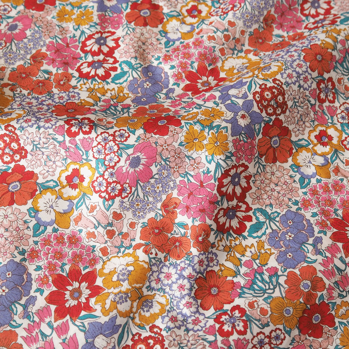 A close-up of a draped fabric with a dense, multicolor floral print featuring red, pink, orange, purple, and yellow flowers on a light background.