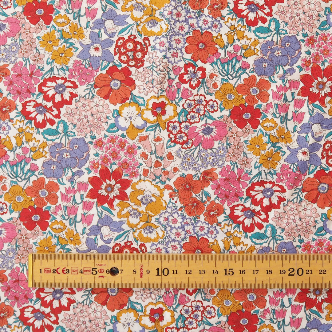 A close-up of a draped fabric with a dense, multicolor floral print featuring red, pink, orange, purple, and yellow flowers on a light background.