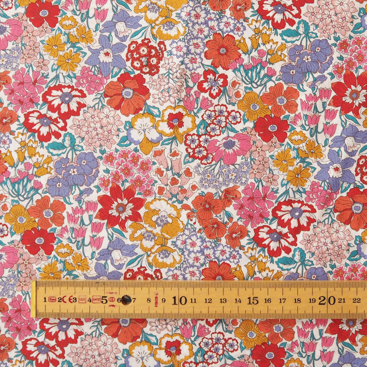 A close-up of a draped fabric with a dense, multicolor floral print featuring red, pink, orange, purple, and yellow flowers on a light background.