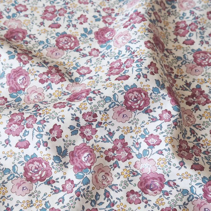 A close-up of draped fabric featuring a vintage-style floral print with pink and mauve roses, blue leaves, and small yellow flowers on an off-white background.