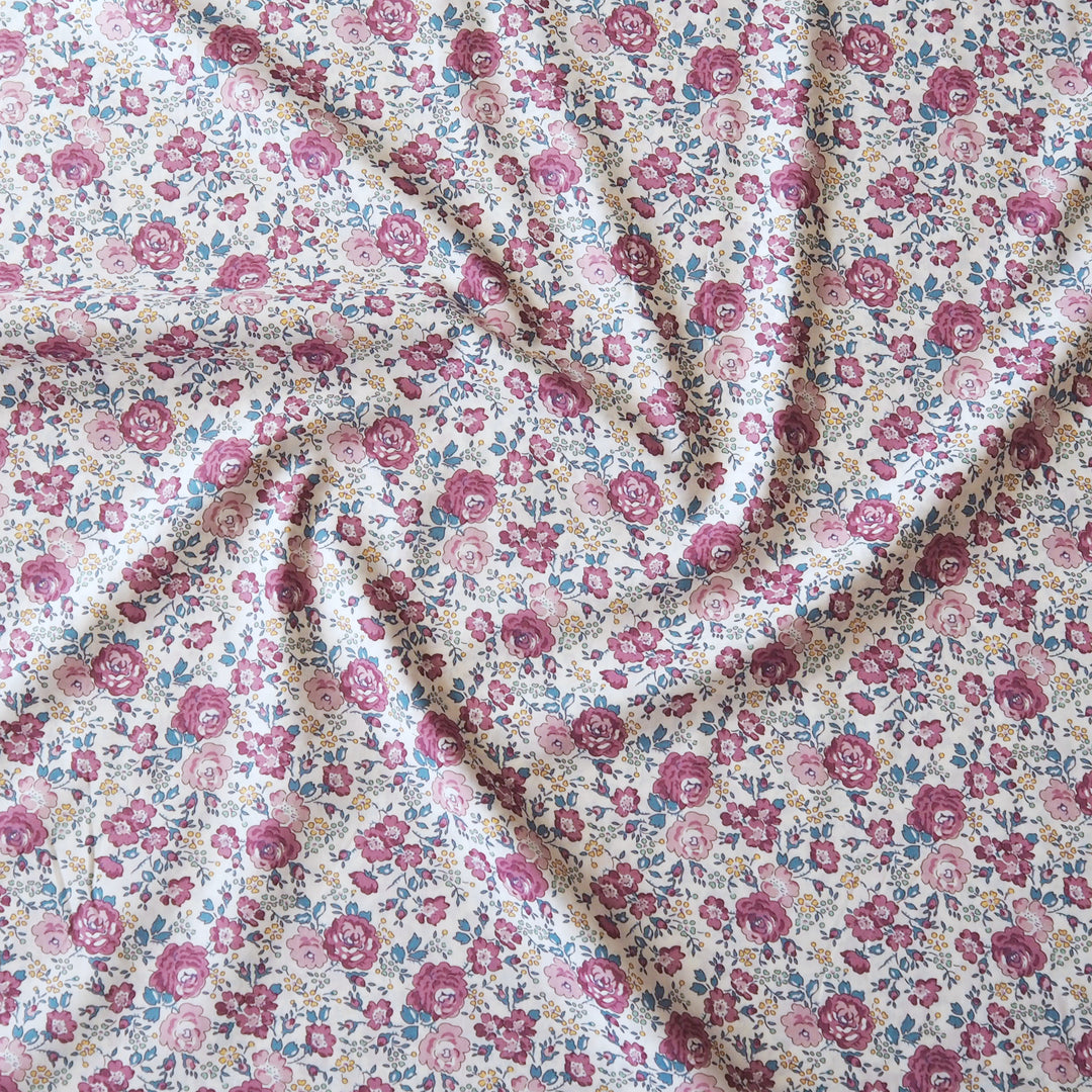 A close-up of a floral fabric with a dense pattern of pink, red, and blue flowers on a cream background, draped in soft folds.