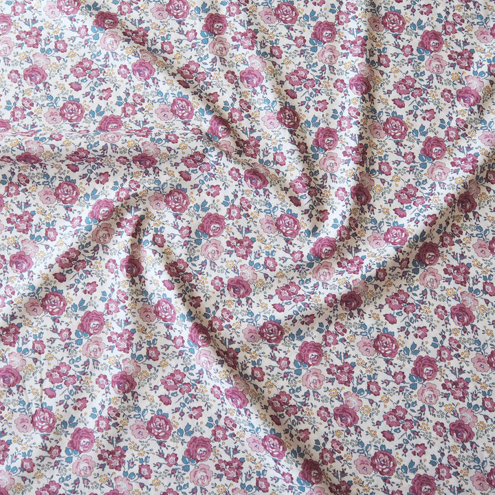 A close-up of a floral fabric with a dense pattern of pink, red, and blue flowers on a cream background, draped in soft folds.