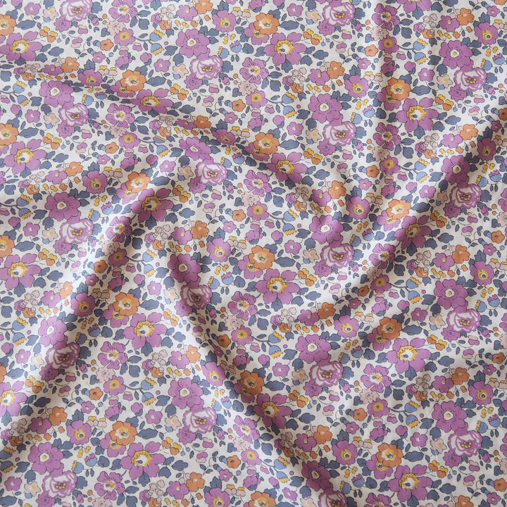 A close-up of a draped fabric with a dense, small-scale floral print. The pattern features purple, pink, orange, and yellow flowers with blue-gray leaves on a white background.