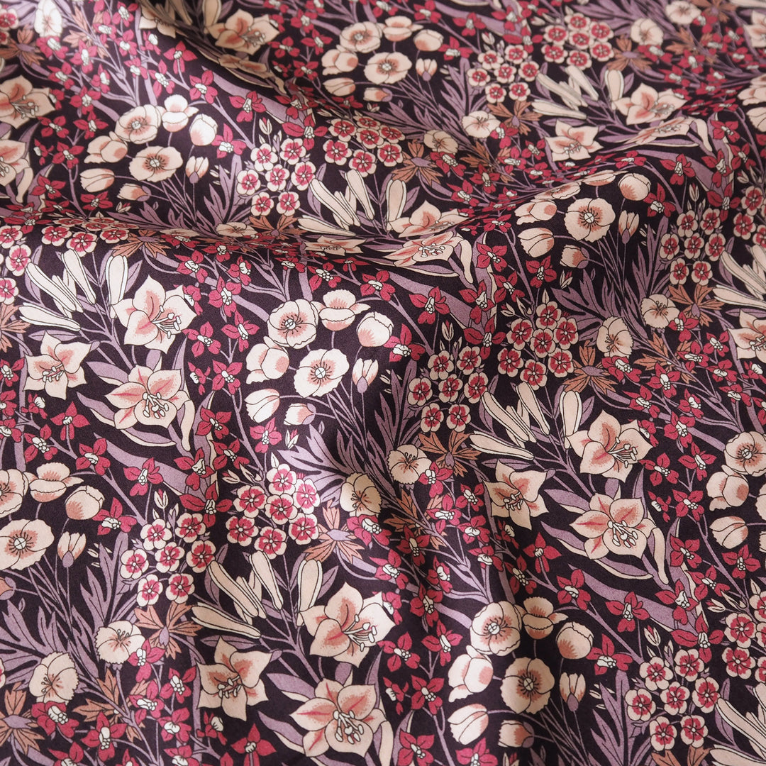 A close-up of draped fabric featuring an intricate floral pattern with pink, cream, and red blossoms on a dark purple background.