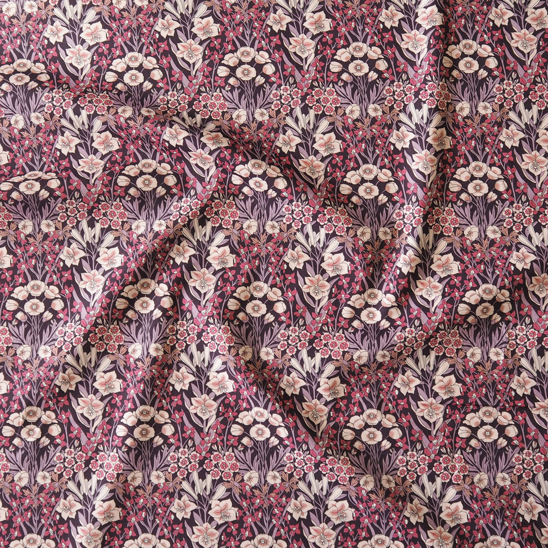 A close-up of draped fabric featuring a dense floral and botanical pattern in muted pink, cream, olive green, and dark plum tones.