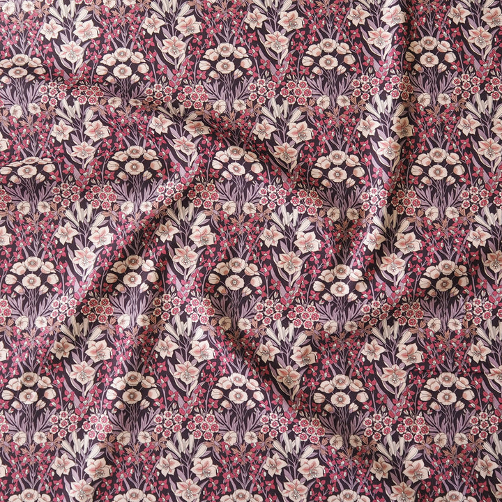 A close-up of draped fabric featuring a dense floral and botanical pattern in muted pink, cream, olive green, and dark plum tones.