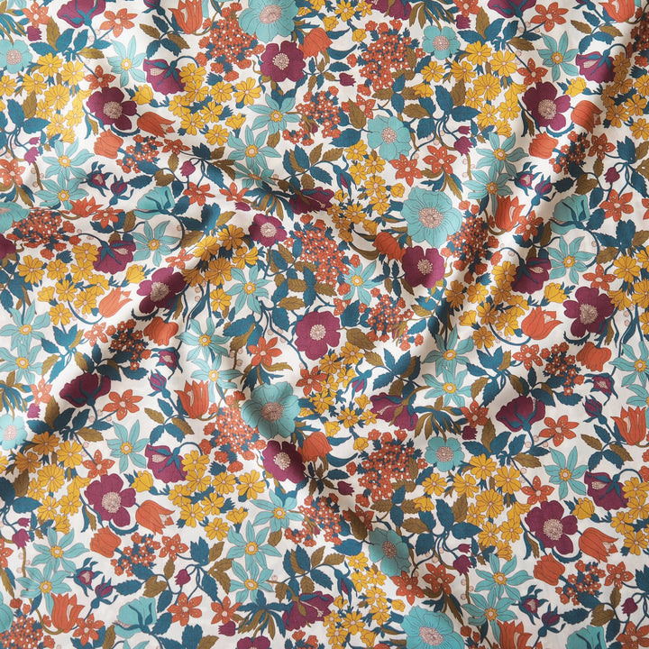 A close-up of a white fabric with a dense, multicolor floral pattern featuring yellow, orange, teal, purple, and red flowers with green and brown leaves.