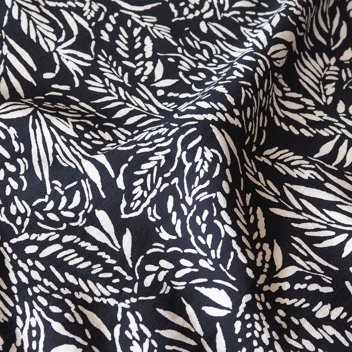 Deep navy and white block-printed fabric with a leafy botanical pattern, shown in soft folds.
