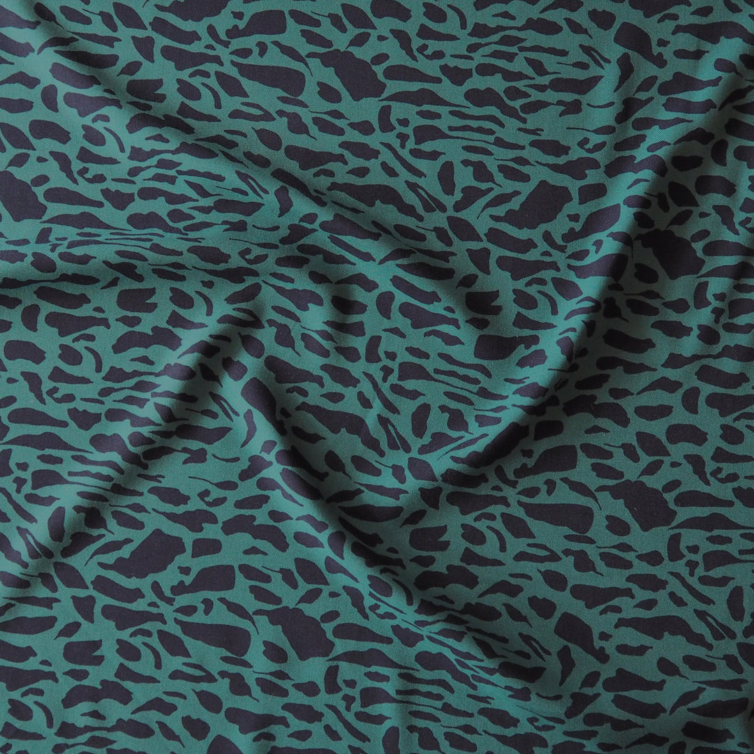 A close-up of draped fabric with an allover irregular spotted pattern in dark teal.