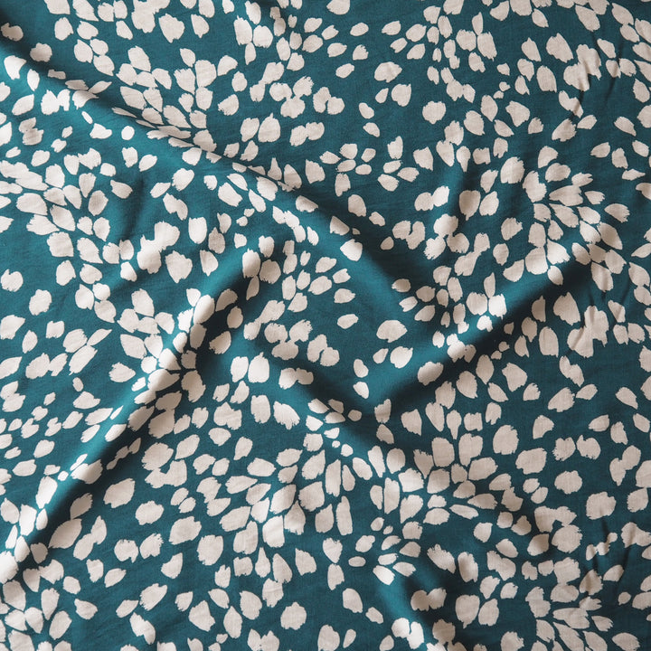 A close-up of draped fabric with a dark teal background and an all-over irregular off-white floral or leaf-like print.
