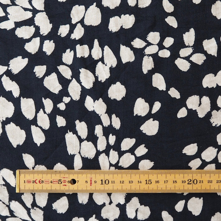 A close-up of a navy blue fabric with a white abstract floral or petal-like print, with a wooden ruler along the bottom edge showing measurements.