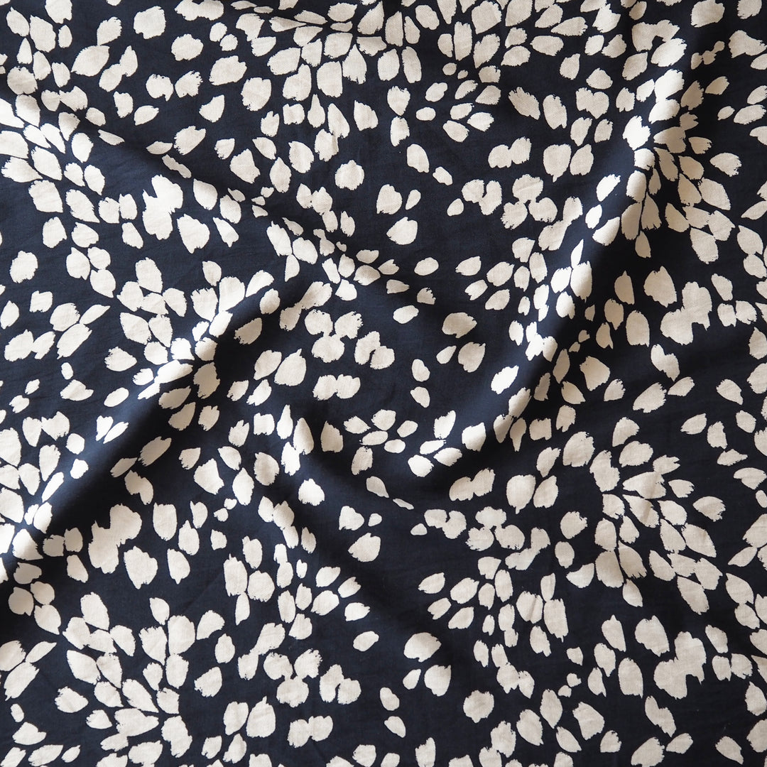 A close-up of draped fabric with a dark navy blue background and an all-over irregular off-white floral or petal-like print.