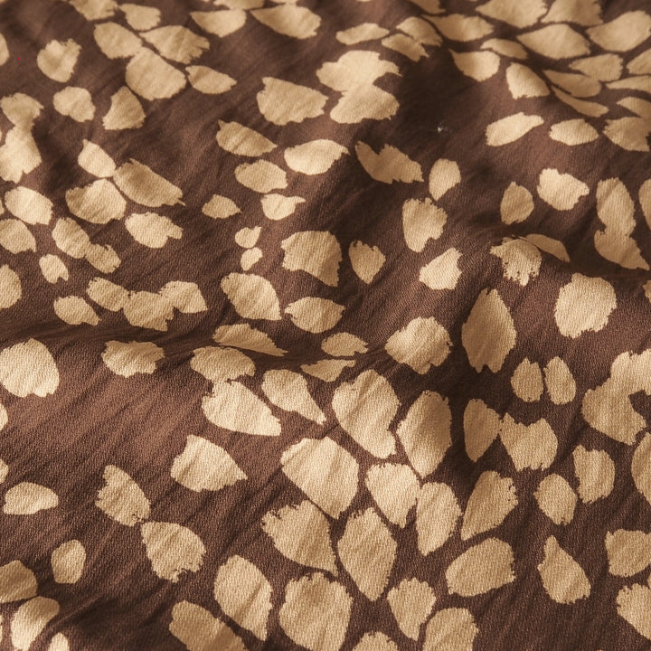 A close-up of a brown fabric with a beige irregular spotted pattern, resembling animal print or a leopard print.