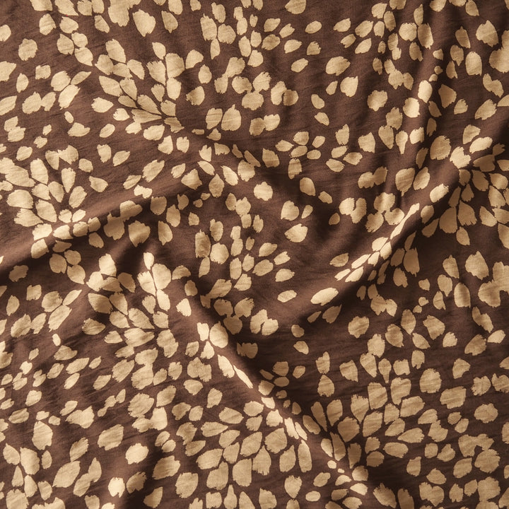 Brown fabric with a beige abstract leopard or watercolor spot pattern, shown with soft folds.