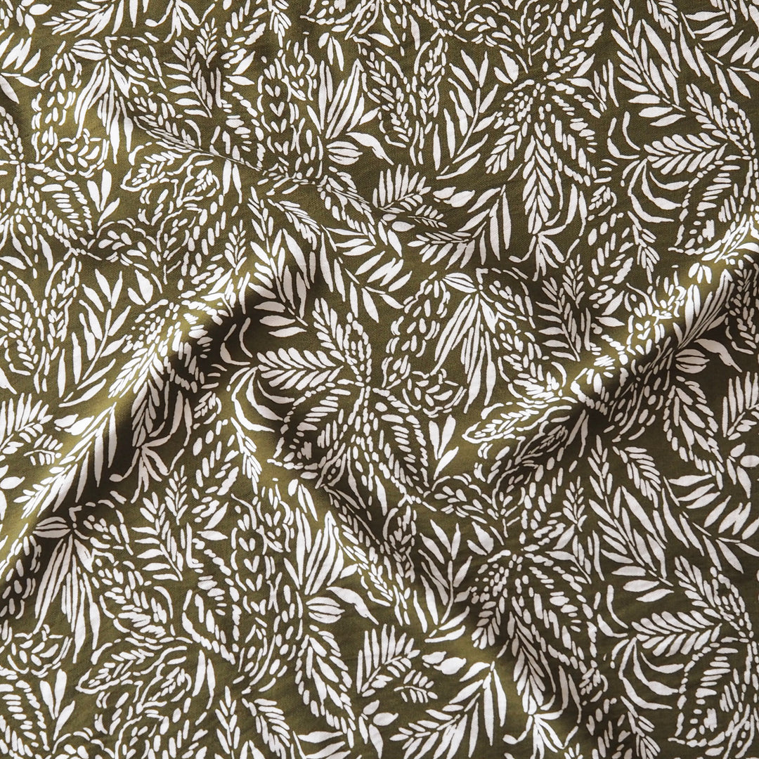 A close-up of a draped fabric with an all-over botanical leaf pattern in white on an olive green background.